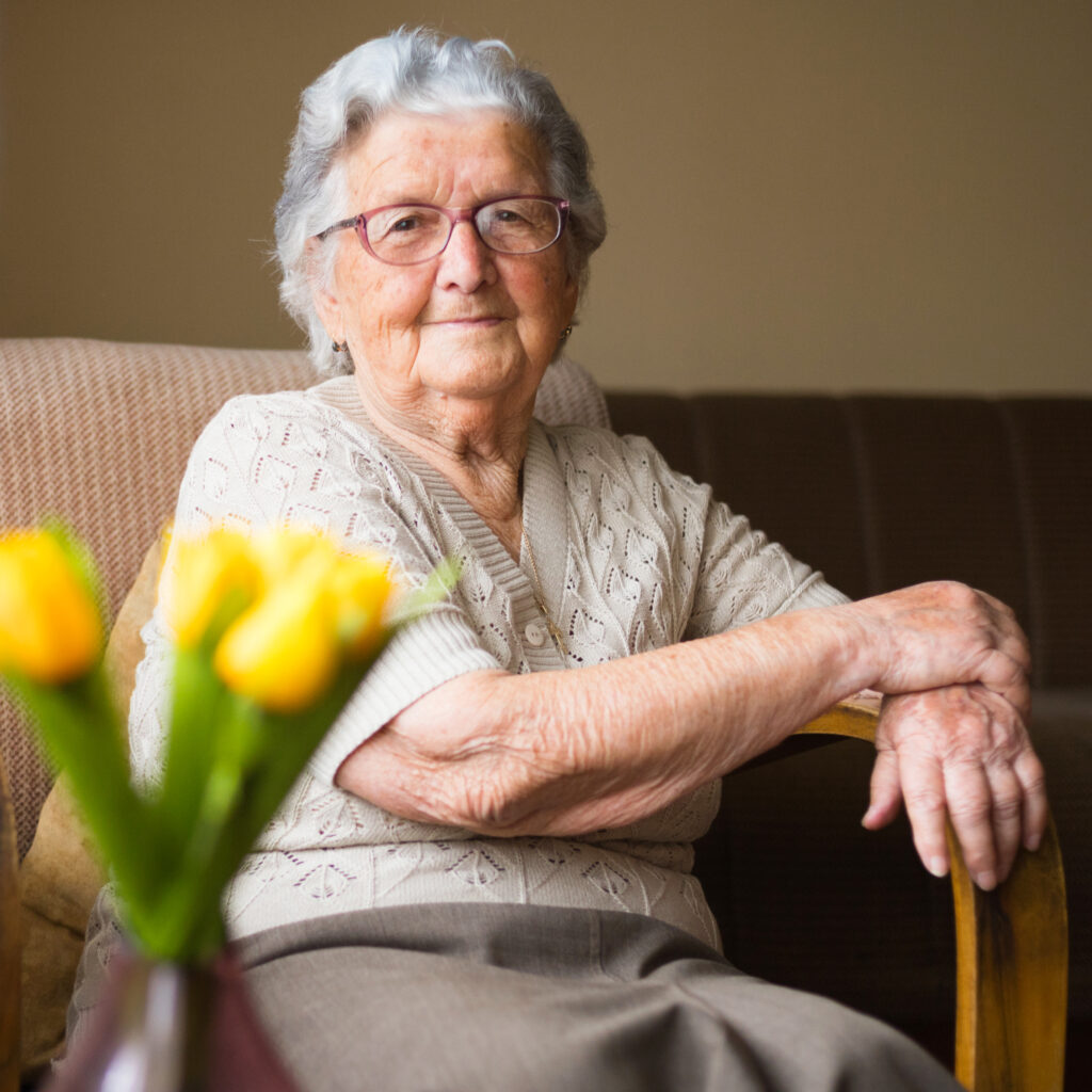 Older Woman smiling on couch with flowers